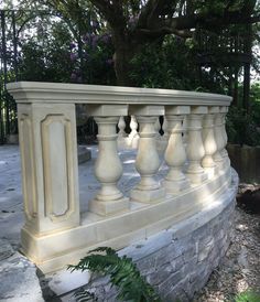 a white stone balcony with columns and railings in the middle of a garden area