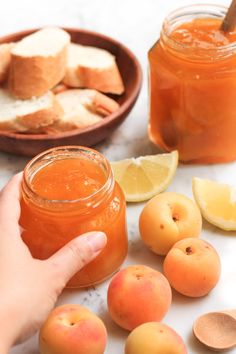 a person is holding a jar of peach jam next to some lemons and bread