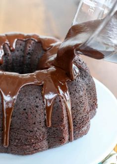 someone pouring chocolate sauce on top of a bundt cake