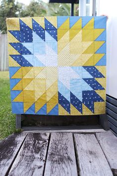 a blue and yellow quilt sitting on top of a wooden table next to a building