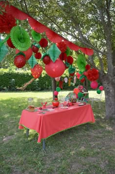 a red table topped with lots of paper lanterns under a canopy covered in pom - poms