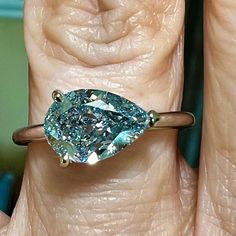 a woman's hand holding a ring with a large blue diamond in the center