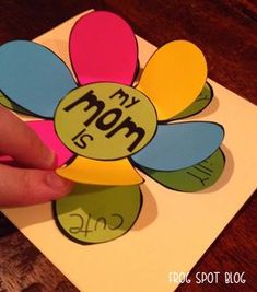 a person holding up a flower shaped card with the word mom on it's side