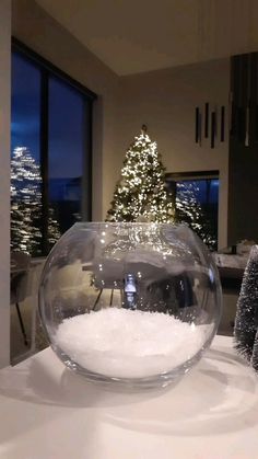 a bowl filled with snow sitting on top of a table next to a christmas tree