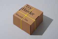 a brown box with yellow ribbon and the words try harder on it sitting on a gray surface