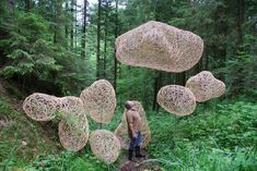 a man standing in the middle of a forest with lots of wire sculptures hanging from it's sides