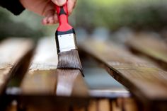 a person holding a paint brush on top of a wooden table with wood slats