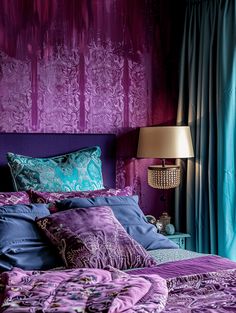 a bed with purple and blue comforters in a bedroom next to a lamp on a table