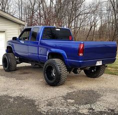 a blue pick up truck parked in front of a house with large tires on it