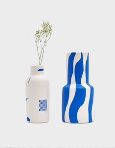 two white and blue vases sitting next to each other, one with a flower in it