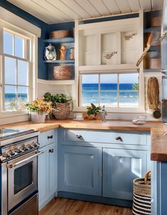 a kitchen with blue cabinets and wooden floors next to an ocean front window, along with baskets on the shelves