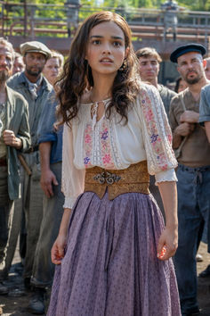 a woman standing in front of a group of people wearing long skirts and blouses