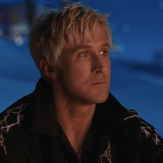 a man with blonde hair wearing a black shirt and looking off to the side in front of a blue background