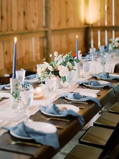 the table is set with blue and white place settings, silverware, and candles