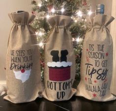 three wine bags decorated with holiday sayings and a christmas tree in the back ground