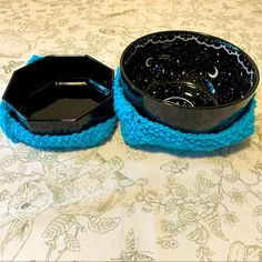 two black bowls sitting on top of a table covered in blue crocheted material