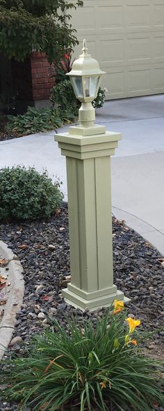 a light green lamp post sitting in the middle of a flower bed next to a driveway