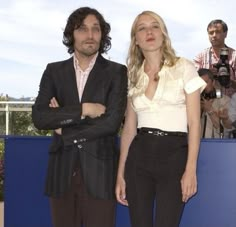 a man and woman standing next to each other in front of a blue wall with cameras