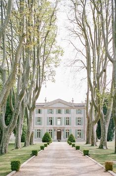 a large white house surrounded by trees and hedges in the middle of a park area