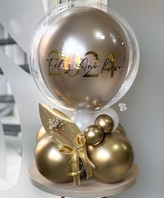 a christmas ornament with gold balls and ribbons on a wooden stand in front of a white wall