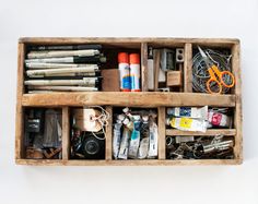 a wooden box filled with lots of crafting supplies on top of a white wall