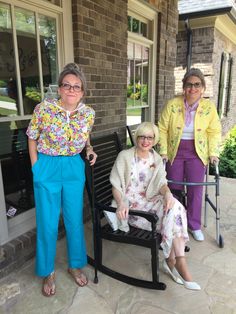 three older women are sitting on a porch chair and one is holding a cane while the other woman stands next to her