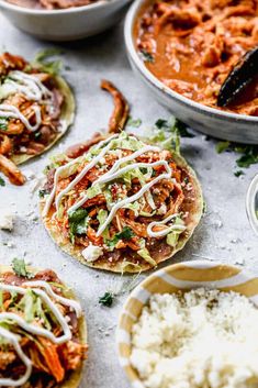 several tacos with shredded cheese and sauce in bowls next to other food on the table