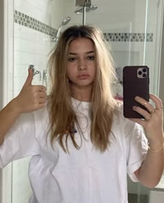 a woman taking a selfie in front of a bathroom mirror with her cell phone