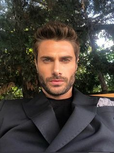 a close up of a person wearing a suit and tie with trees in the background