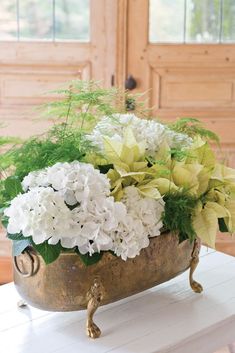 a metal bowl filled with white and green flowers on top of a wooden table next to a dresser