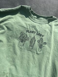 Channel your inner green thumb with our Plant Lady Tee. Made from soft, organic cotton, this shirt worn proudly displays your love for all things botanical. Perfect for brunch, gardening, or just lounging in the sun. Embrace your plant obsession in style. (Gardening gloves not included!) Garden T Shirt, Plant Shopping Outfit, Plant Tshirts, Fall Merch, Plant Obsession, Merch Ideas, Market Ideas, Botanical Shirt, Gardening Shirts