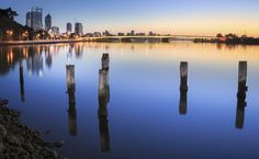 a body of water with some wooden posts in the foreground and a cityscape in the background