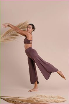 a woman with long hair standing on one leg in the air and wearing wide legged pants