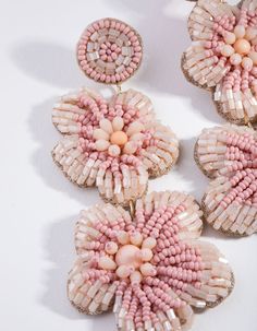 three pairs of pink and white beaded flower earrings on a white surface with beads