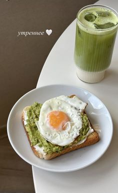 an egg and avocado toast on a white plate next to a green smoothie