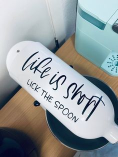 a white sign that says wake is sweet lick the spoon on top of a frying pan