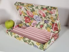 an apple sitting on top of a table next to a flowered box with compartments