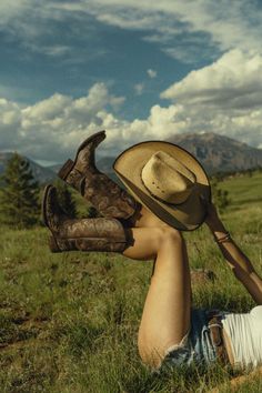 a person laying in the grass with a cowboy hat on their head and boots over their face