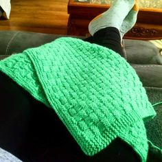 someone is sitting on the couch with their feet up and wearing green knitted blanket