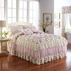 a bed with pink and white ruffled bedspread on top of it in a bedroom