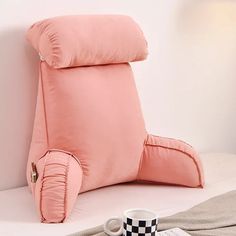 a pink pillow sitting on top of a bed next to a cup