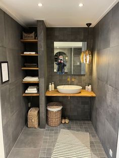 a bathroom with gray walls and tile flooring is pictured in this image, there is a large mirror on the wall above the sink