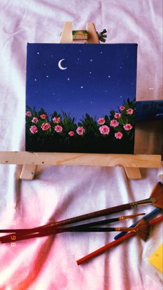 an easel with flowers and paintbrushes sitting on top of it next to a painting