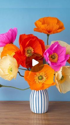 a vase filled with colorful flowers on top of a wooden table next to a blue wall