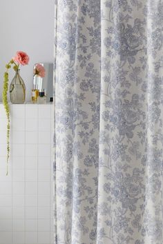 a white and blue shower curtain next to a bath tub with flowers on the side