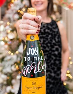 a woman holding a bottle of champagne in front of a christmas tree