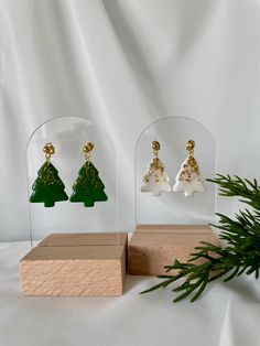 three small christmas trees are displayed in glass cases on a white surface with pine branches