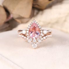 a pink diamond and pearl ring sitting on top of a white cloth