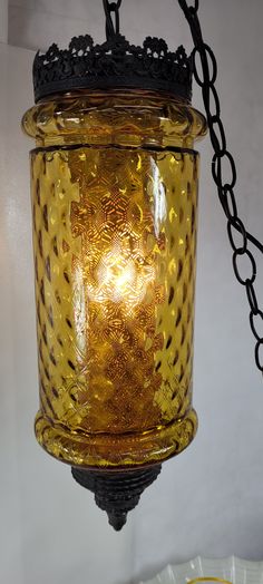 a yellow glass lantern hanging from a chain in a room with a plate on the floor