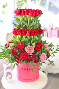 there is a pink box with red roses in it on top of a white table